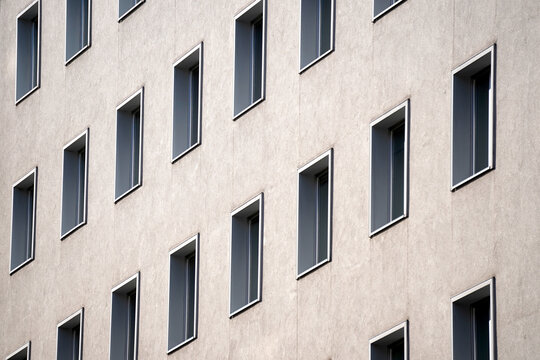 Minimalist building facade with evenly spaced rectangular windows. Repetitive architectural geometry under daylight. Urban symmetry highlights clean modern design concept.

