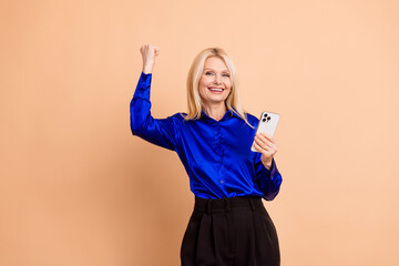 Confident businesswoman raising a fist in success holding a phone wearing a blue blouse against a...