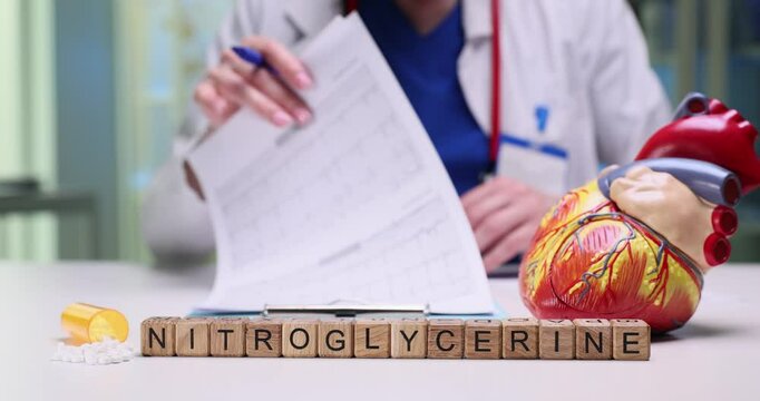 A healthcare professional reviews paperwork for nitroglycerin with a detailed heart model on the table