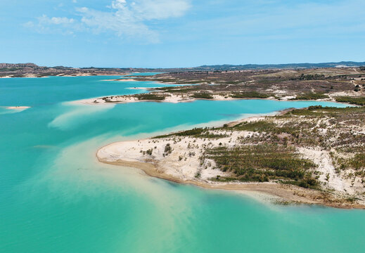 Aerial view of Embalse de La Pedrera reservoir landscape, with striking turquoise waters, curving white-sand shores, and desert-like hills in distance. Costa Blanca. Province of Alicante. Spain