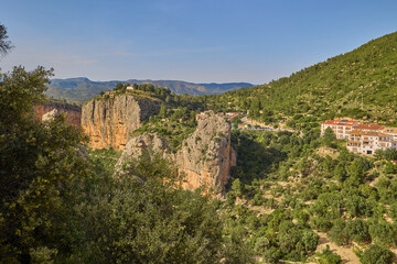 Mountain village with houses, cliffs, and lush green hills on a sunny day