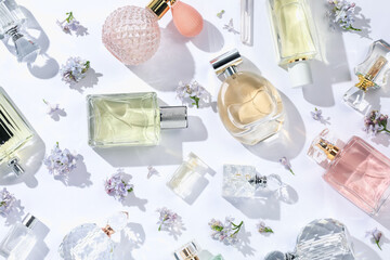 Luxury perfumes and beautiful lilac flowers on white background, flat lay