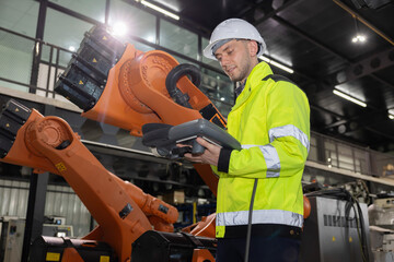 Caucasian worker operates industrial robot arm in a modern factory while looking and smiling to camera