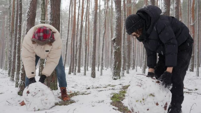 Two brothers work in parallel, demonstrating teamwork and synergy as they build a snowman. This joint effort showcases a strong partnership and dedication to achieving a shared creative goal.