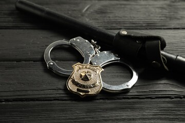 Police badge, handcuffs and baton on black wooden table, closeup