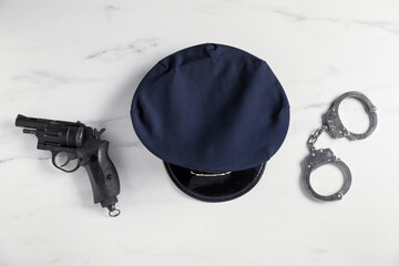 Police cap, gun and handcuffs on white marble table, flat lay