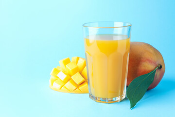 Tasty mango juice in glass and fresh fruits on light blue background, space for text