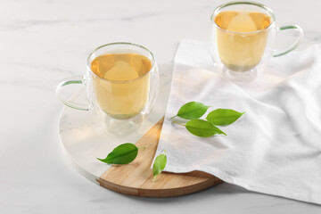 Tasty green tea in glass cups and leaves on white marble table