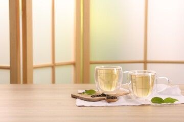 Tasty green tea in glass cups, brew and leaves on wooden table indoors, space for text
