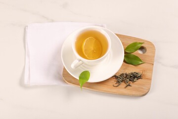 Tasty green tea with lemon in cup, brew and leaves on white marble table, above view