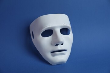 One white theatre mask on blue background, above view