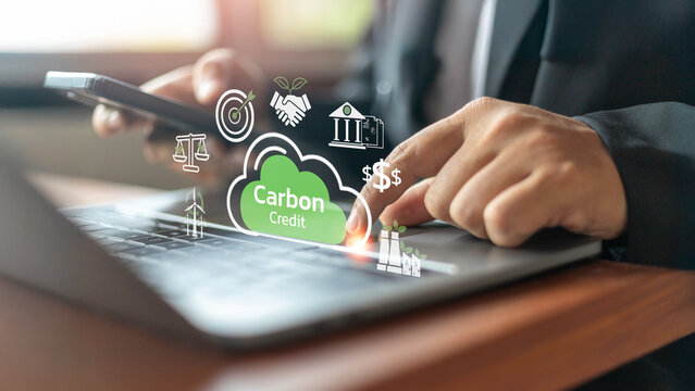 A businessperson uses a smartphone and a laptop to access a carbon credit platform.