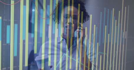 Talking on smartphone adult African American woman holding coffee cup in office, with data charts