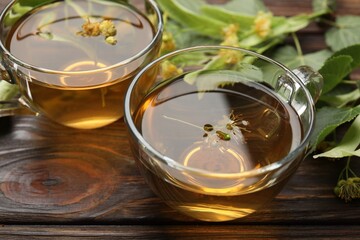 Fresh linden tea in cups and flowers on wooden table, closeup