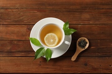 Tasty green tea with lemon in cup, brew and leaves on wooden table, flat lay