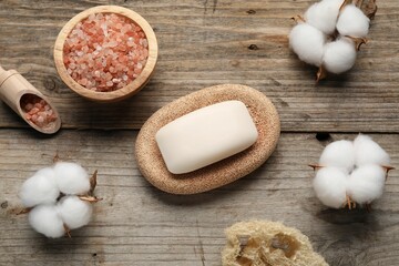 Soap bar, sea salt, loofah sponge and cotton flowers on wooden table, flat lay