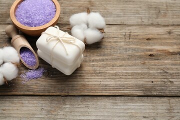 Soap bars, sea salt and cotton flowers on wooden table, above view. Space for text