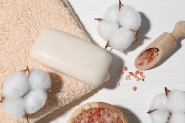 Soap bar, sea salt, cotton flowers and towel on white wooden table, flat lay