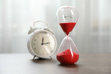 Deadline. Hourglass with flowing sand and alarm clock on wooden table indoors