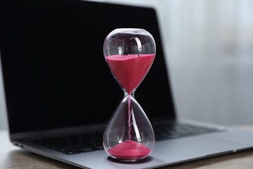 Deadline. Hourglass with flowing sand and laptop on table indoors, closeup