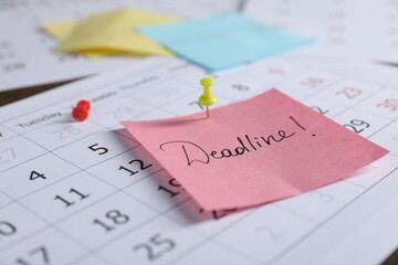 Sticky note with word Deadline and calendar on table, closeup