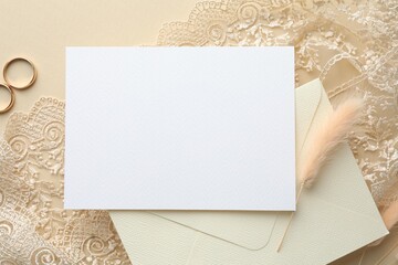 Wedding invitation card, envelope, golden rings, lace ribbon and dry spikes on beige background, flat lay