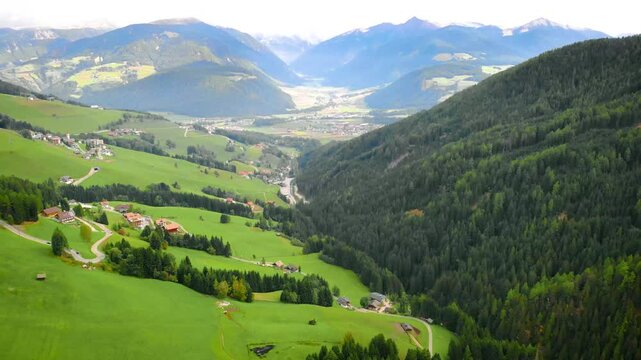 Aerial view. video with a drone. Beautiful fabulous dolomite alpine mountains with green forest, blue sky. fly shooting. Top view of ethnic settlement village, meadow field grass. Tourism, rest Italy