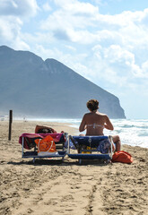 Two women relaxing on beach chairs facing the ocean with a scenic mountain in the background....