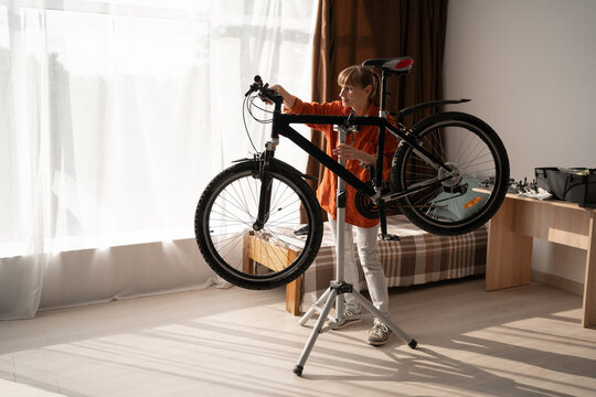 Active cyclist doing bike maintenance routine at home. Middle-aged woman examining damaged bicycle