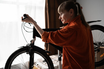 Active cyclist doing bike maintenance routine at home. Middle-aged woman examining damaged bicycle