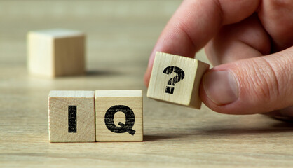 A hand holding a wooden block with an IQ question mark, symbolizing intelligence and cognitive assessment in a minimalistic setting with natural light.