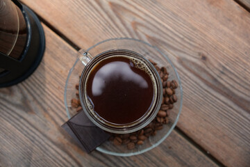 cup of coffee on wooden table with a piece of chocolate on the side