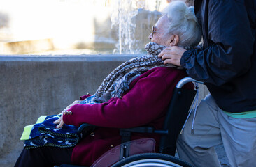 An elderly woman in a wheelchair warmly dressed, being gently cared for by a younger person...