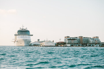 Cruise ship docked at a coastal harbor near modern buildings under clear skies