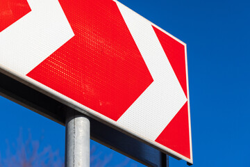 A red directional road sign with white chevrons pointing to the right