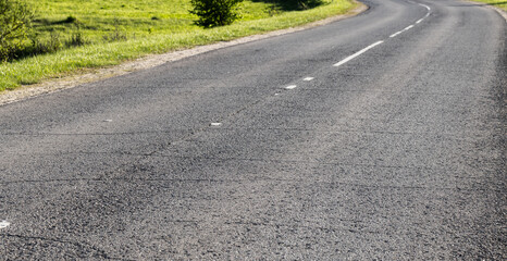An empty curved asphalt road stretches through a lush green countryside