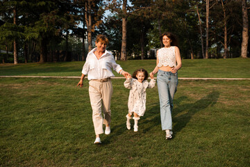 Obraz premium Happy family with child girl with mother and granny running in park with green grass lawn outdoors. Childhood.