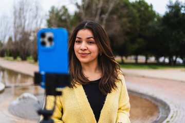 Young woman vlogger creating video content for social media using a smartphone and tripod in an urban park setting
