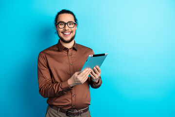 Young businessman smiling confidently while holding a tablet against a teal background, showcasing...