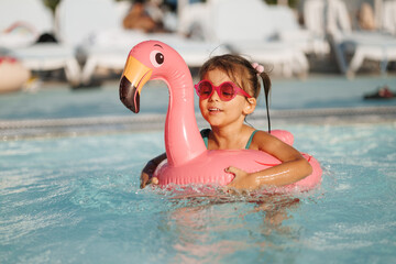 Cute funny toddler girl in a sunglasses relaxing on inflatable toy ring floating in pool have fun during summer vacation. Child having fun in swimming pool. 