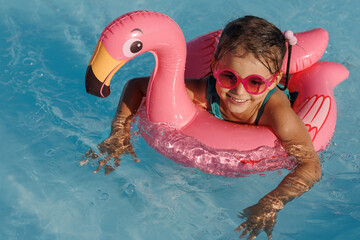 Cute funny toddler girl in a sunglasses relaxing on inflatable toy ring floating in pool have fun during summer vacation. Child having fun in swimming pool. 