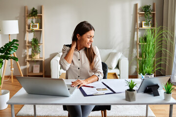 Freelancer feeling neck pain while working on a laptop at home