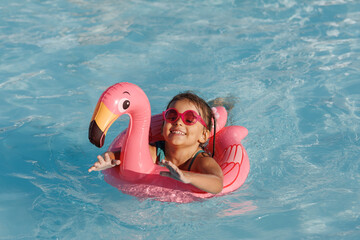 Cute funny toddler girl in a sunglasses relaxing on inflatable toy ring floating in pool have fun during summer vacation. Child having fun in swimming pool. 
