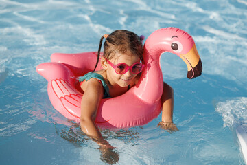 Cute funny toddler girl in a sunglasses relaxing on inflatable toy ring floating in pool have fun during summer vacation. Child having fun in swimming pool. 