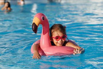 Cute funny toddler girl in a sunglasses relaxing on inflatable toy ring floating in pool have fun during summer vacation. Child having fun in swimming pool. 
