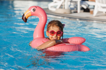 Cute funny toddler girl in a sunglasses relaxing on inflatable toy ring floating in pool have fun during summer vacation. Child having fun in swimming pool. 
