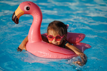 Cute funny toddler girl in a sunglasses relaxing on inflatable toy ring floating in pool have fun during summer vacation. Child having fun in swimming pool. 