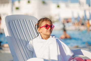 Funny little girl relaxing on summer vacation. The child has fun on the beach. Cute baby in a colorful swimsuit and sunglasses is resting.