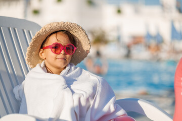 Funny little girl relaxing on summer vacation. The child has fun on the beach. Cute baby in a colorful swimsuit and sunglasses is resting.