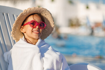 Funny little girl relaxing on summer vacation. The child has fun on the beach. Cute baby in a colorful swimsuit and sunglasses is resting.
